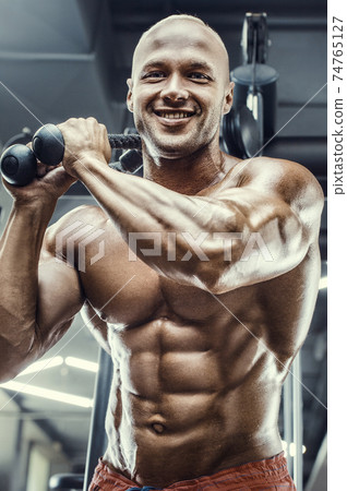 Bodybuilder strong man pumping up abs muscles Bodybuilder strong man pumping up abs muscles 74765127