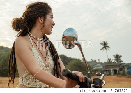 A woman sits on a motorcycle in a field 74765271
