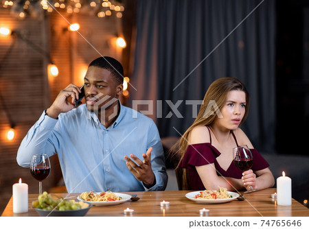 Young Woman Feeling Annoyed While Her Boyfriend Talking On Cellphone During Date Young Woman Feeling Annoyed While Her Boyfriend Talking On Cellphone During Date 74765646