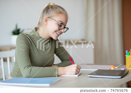 Smiling teen girl studying at home and using laptop 74765676