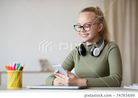 Cheerful teenager blonde girl using smartphone at home Cheerful teenager blonde girl using smartphone at home 74765699
