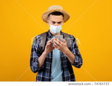Young traveler in face mask having difficulty booking tour or hotel online during covid lockdown, orange background Young traveler in face mask having difficulty booking tour or hotel online during covid lockdown, orange background 74765737