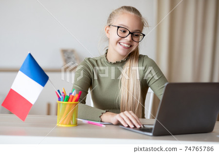 Cheerful girl with flag of France using laptop 74765786