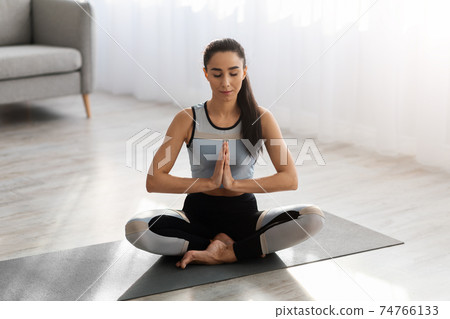 Peaceful sporty woman meditating at home, sitting in lotus asana Peaceful sporty woman meditating at home, sitting in lotus asana 74766133