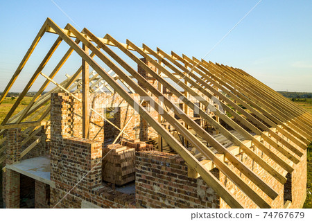 Unfinished brick house with wooden roof structure under construction. 74767679
