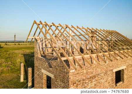 Unfinished brick house with wooden roof structure under construction. 74767680