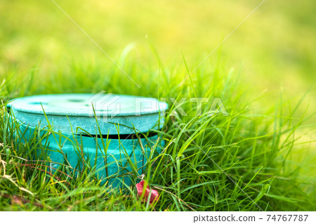 Closeup of green plastic pipe with cover on green grass lawn. 74767787