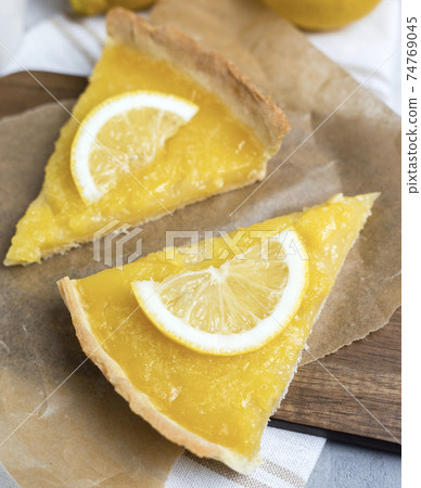 Two pieces of lemon tart with slice of lemons closeup on stone background, top view, copy space. Two pieces of lemon tart with slice of lemons closeup on stone background, top view, copy space. 74769045