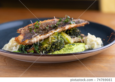 Grilled sea bass with broccoli and pea puree on a wooden table Grilled sea bass with broccoli and pea puree on a wooden table 74769081