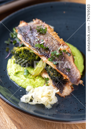 Grilled sea bass with broccoli and pea puree on a wooden table Grilled sea bass with broccoli and pea puree on a wooden table 74769083