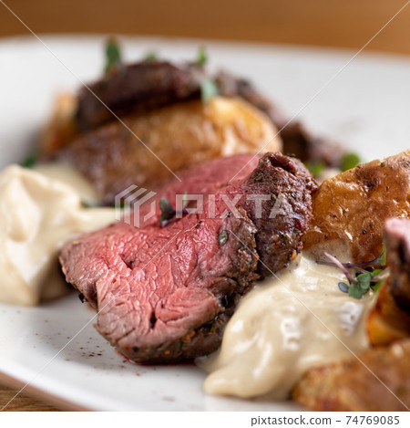 fillet of Mignon on a black plate on a background of greens, spices and vegetables, on a copper sheet. close up fillet of Mignon on a black plate on a background of greens, spices and vegetables, on a copper sheet. close up 74769085