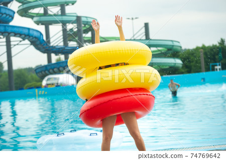a woman in a swimsuit with rubber inflatable circles plays and has a good time near the pool of the summer water park a woman in a swimsuit with rubber inflatable circles plays and has a good time near the pool of the summer water park 74769642
