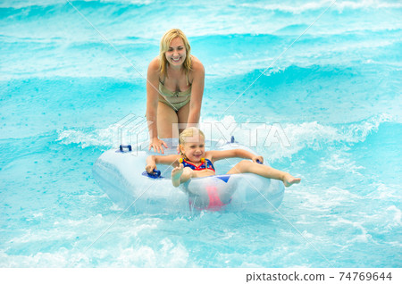 a woman with a child in a rubber inflatable circle plays in the pool of a summer water park in the rain a woman with a child in a rubber inflatable circle plays in the pool of a summer water park in the rain 74769644