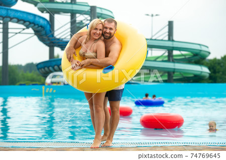 a man and a woman in a rubber inflatable circle stand against the background of a summer water park pool 74769645