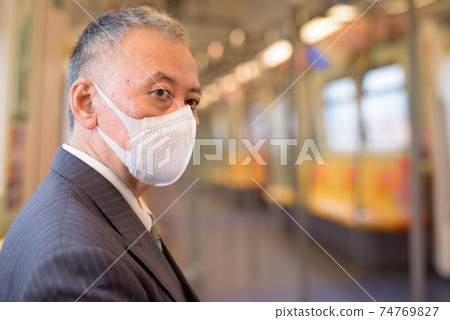 Mature Japanese businessman with mask thinking and sitting with distance inside the train 74769827