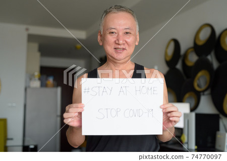 Happy mature Japanese man holding Stay At Home sign while under quarantine due to covid-19 pandemic Happy mature Japanese man holding Stay At Home sign while under quarantine due to covid-19 pandemic 74770097