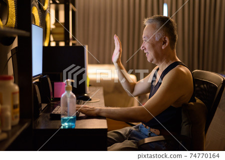 Happy mature Japanese man video calling with computer at home Happy mature Japanese man video calling with computer at home 74770164