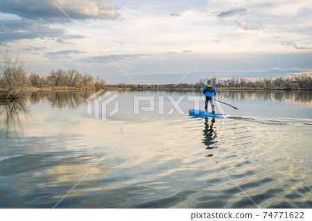 Paddling stand up paddleboard on a calm lake Paddling stand up paddleboard on a calm lake 74771622