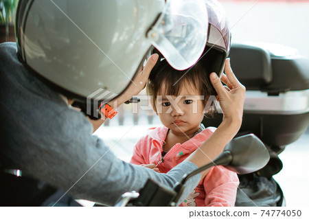 the baby looks at the camera while wearing a helmet assisted by the mother the baby looks at the camera while wearing a helmet assisted by the mother 74774050