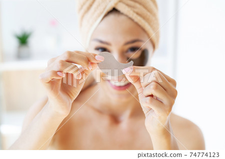 Young woman with beautiful skin puts black patches on her face 74774123
