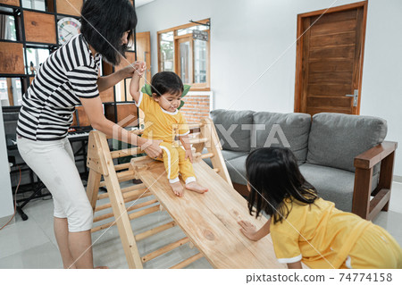 a woman patiently holding a baby while standing sliding on a pikler triangle toy a woman patiently holding a baby while standing sliding on a pikler triangle toy 74774158