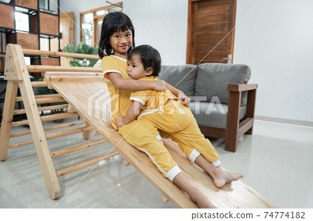 The siblings hug while playing slide in the Pikler Triangle Toy together The siblings hug while playing slide in the Pikler Triangle Toy together 74774182