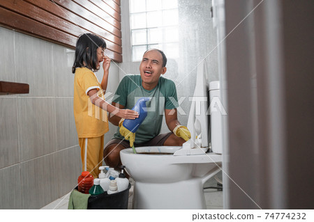 the little girl in a nasty pose holding a bottle of cleaning fluid chatting with her dad while brushing the dirty toilet the little girl in a nasty pose holding a bottle of cleaning fluid chatting with her dad while brushing the dirty toilet 74774232
