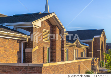 Church exterior with red brick wall and shingles on the roof against blue sky 74774382