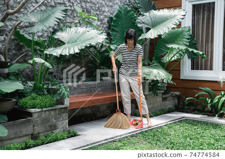 housewife cleaning a yard with sweeping the leaves housewife cleaning a yard with sweeping the leaves 74774584