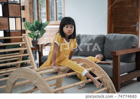 a girl sits on a pikler climbing toy with a baby in the background playing on the sofa a girl sits on a pikler climbing toy with a baby in the background playing on the sofa 74774680