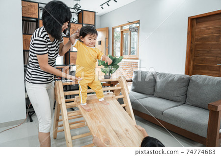 a mother patiently holds the baby's hand while standing sliding on a pikler triangle toy a mother patiently holds the baby's hand while standing sliding on a pikler triangle toy 74774683