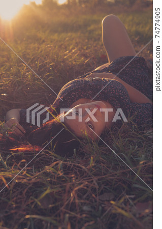 Nice smiling brunette girl relaxing on the grass in the park 74774905