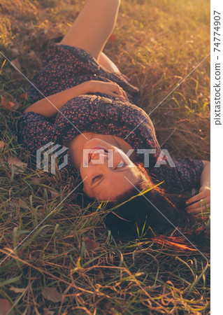 Jollyful lady lying in the park on autumnal grass and looking at camera. 74774907