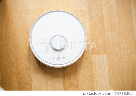 Smart House. Vacuum cleaner robot runs on wood floor in a office Smart House. Vacuum cleaner robot runs on wood floor in a office 74776303