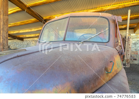 Old vintage car with rusty and dirty exterior inside a garage with metal roof Old vintage car with rusty and dirty exterior inside a garage with metal roof 74776583