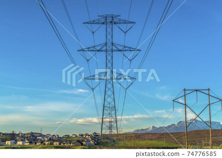High voltage electric transmission tower against homes mountain and blue sky High voltage electric transmission tower against homes mountain and blue sky 74776585