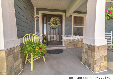 Porch and facade of home decorated with colorful flowers and wreath on the door 74777160