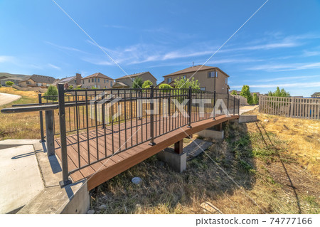 Side view of a bridge over a grassy terrain with homes and blue sky background Side view of a bridge over a grassy terrain with homes and blue sky background 74777166