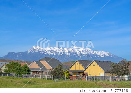 Single storey houses against striking snow capped mountain and vibrant blue sky Single storey houses against striking snow capped mountain and vibrant blue sky 74777168
