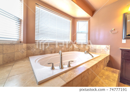 Elevated built in bathtub against the bay windows with blinds of a bathroom 74777191
