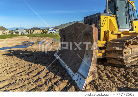 Close up of a bulldozer with metal blade yellow paint and tracks with dried mud Close up of a bulldozer with metal blade yellow paint and tracks with dried mud 74778502