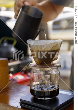 Barista spills hot water prepare filter coffee from stainless steel teapot to drip paper maker on black simple weights. Everything thick wooden table cafe shop. Steam. Process vintage style 74779310
