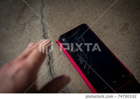 一個人將智能手機放在混凝土上，屏幕破裂 74780192