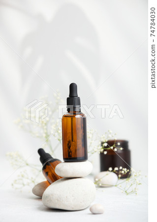 Bottle of dark amber glass with essential oil on stack of natural stones, copy space 74784030