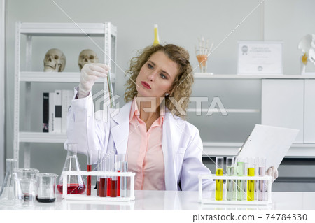 Young blonde scientists are comparing the results of new chemical research with experimental charts on the clipboard. Working atmosphere in chemical laboratory. Young blonde scientists are comparing the results of new chemical research with experimental charts on the clipboard. Working atmosphere in chemical laboratory. 74784330