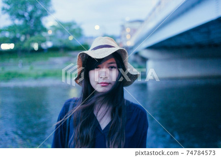 Riverside background Evening, a woman with long hair in a straw hat, looking at the camera Riverside background Evening, a woman with long hair in a straw hat, looking at the camera 74784573