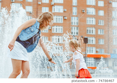 mom plays with her daughter at the fountain 74786467