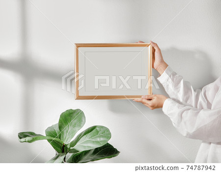 Hand holding Frame or Poster mock up in living room and window shadow on white wall background. 74787942