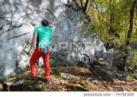 Athletic middle aged male climber stands in front of a large training rock before free mountain climbing in the forest in autumn Athletic middle aged male climber stands in front of a large training rock before free mountain climbing in the forest in autumn 74792300