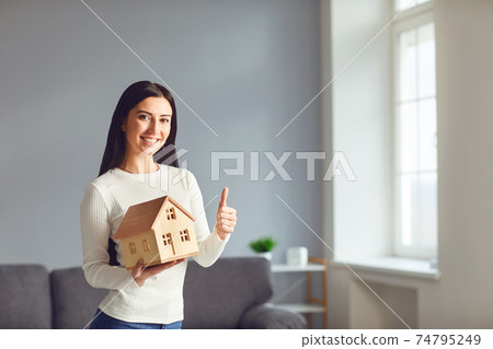 Happy couple holding a mock up of a house in their hands while standing in a room at home. Happy couple holding a mock up of a house in their hands while standing in a room at home. 74795249